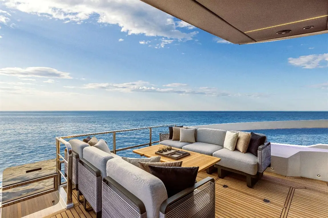 Luxury outdoor seating area with plush cushions, a wooden table, and a stunning ocean view under a clear blue sky.